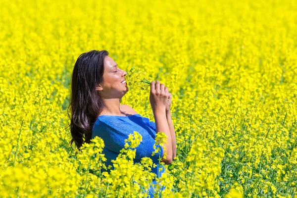 Mujer joven huele flores amarillas en campo de colza — Foto de Stock