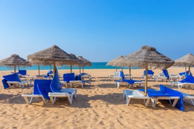 Grup hasır plaj şemsiyeleri ve Portekiz sahillerindeki mavi plaj yatakları.