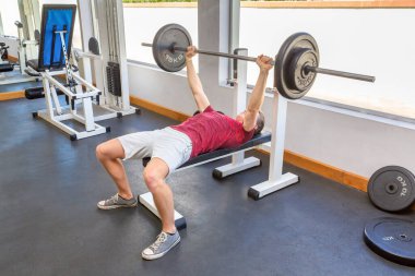 Genç Hollandalı adam spor salonunda halterle ağırlık kaldırıyor.