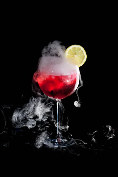 Una taza de cóctel rojo frío con humo de hielo seco y una rodaja de limón — Foto de Stock