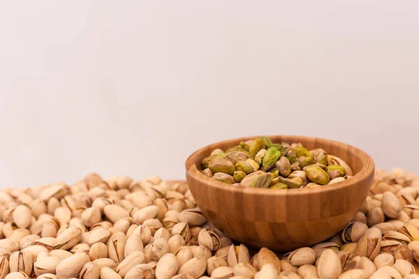 Cáscara y pistachos pelados en cuenco de madera con fondo blanco — Foto de Stock