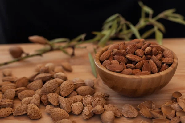 Cáscara y almendras peladas en tazón de madera con un brunch de árbol con fondo negro — Foto de Stock