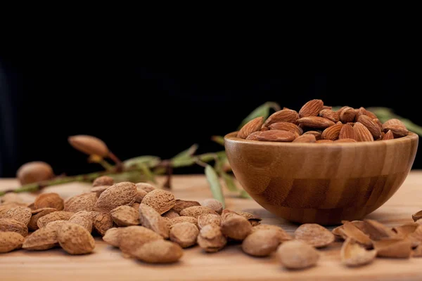 Shell and peeled almonds in wooden bowl with a tree brunch with black background