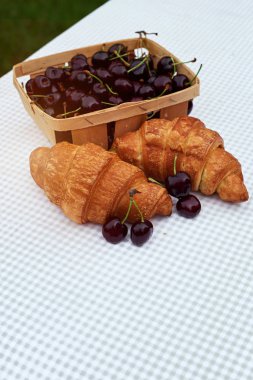 bahar bahçesinde bir masada kruvasan ile bir sepet içinde olgun kiraz