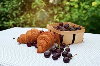 bahar bahçesinde bir masada kruvasan ile bir sepet içinde olgun kiraz