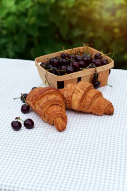 bahar bahçesinde bir masada kruvasan ile bir sepet içinde olgun kiraz