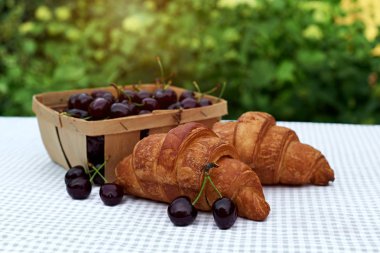 bahar bahçesinde bir masada kruvasan ile bir sepet içinde olgun kiraz