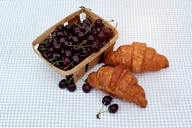 bahar bahçesinde bir masada kruvasan ile bir sepet içinde olgun kiraz
