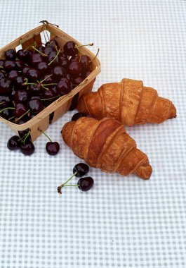 bahar bahçesinde bir masada kruvasan ile bir sepet içinde olgun kiraz