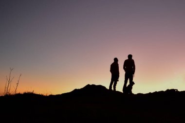 Oğluyla birlikte bir sırtta köpekleriyle güneşin doğuşunu izleyen bir baba