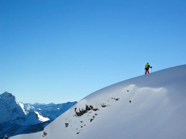 Scogliera sotto la neve di fronte ad un panorama montano in inverno nelle Alpi austriache, con uno sciatore in cima . — Foto Stock