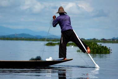 Lake Inle, Myanmar /Birma'da eski teknesini tek ayağıyla sürerken ağıyla çalışan geleneksel balıkçı.