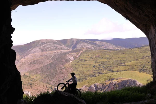 WITH A MOUNTAIN BIKE IN A LARGE CAVE IN FRONT OF A LARGE VALLEY