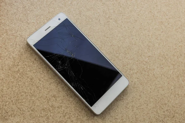 Modern touch screen smartphone with broken screen isolated on stone background
