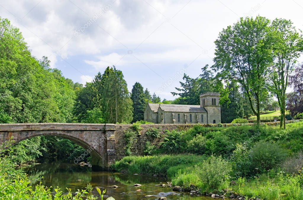 Capturing a quintessentially English village pastoral scene, incorporating Askham Bridge and St Peter's Church, in Askham, Penrith, Cumbria, England.