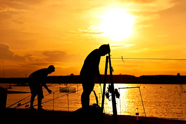 Silhouette of two man fishing on a beautiful lake at sunset.