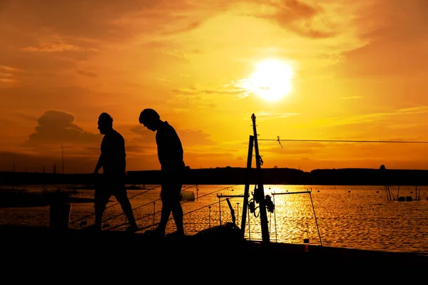 Silhouette de deux hommes pêchant sur un beau lac au coucher du soleil . — Photo