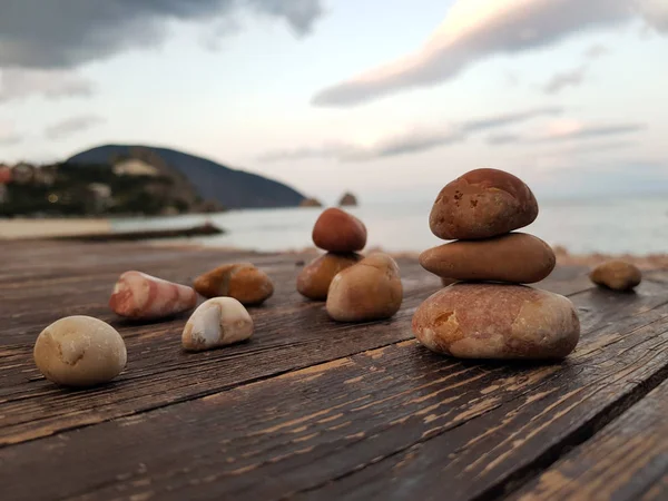Bir deniz manzara arka plan üzerinde dengeli kırmızı kayalar, ahşap bir döşeme, çakıl piramit üzerinde. Denge, uyum ve meditasyon kavramı. Yumuşak odaklama, seçici odaklama