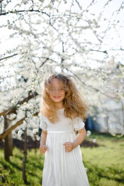  Kıvırcık sarı saçlar çiçek açan bahçede gülümseyen güzel kız.