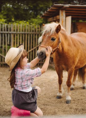 Kahverengi saçlı, kovboy şapkalı, çizmeli, ekose gömlekli, bej atlı, güzel bir kız.
