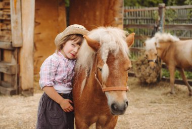Kahverengi saçlı, kovboy şapkalı, çizmeli, ekose gömlekli, bej atlı, güzel bir kız.