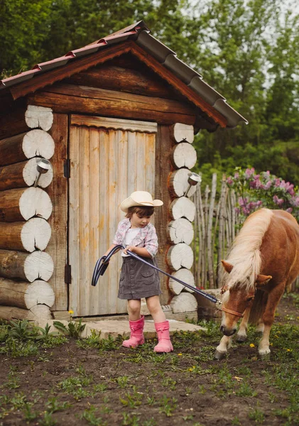 카우보이 모자를 머리의 아름다운 소녀와 베이지 조랑말을 바지를 부츠를 스톡 사진