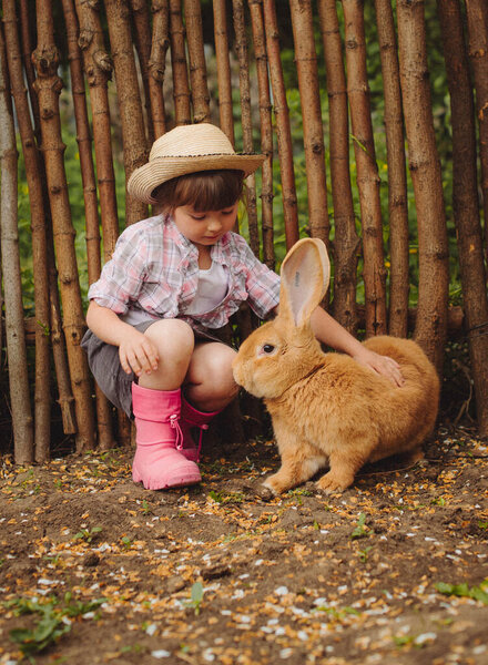 Милая маленькая девочка в ковбойской шляпе с большим кроликом красным кроликом с большими ушами
