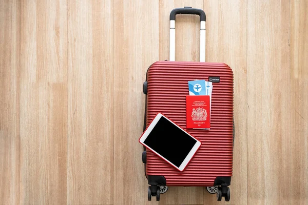 Seyahate çıkmaya hazırlanan ya da yurtdışında çalışmaya hazırlanan şirket çalışanları için ekipman, tablet ve pasaport kırmızı bir bavula yerleştirilip seyahat için hazırlanıyor.