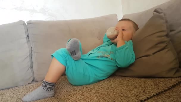 Két éves fiú feküdt a kanapén és csokis tejet ivott, gyerek a családban — Stock videók