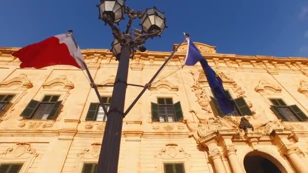 Valletta, Malta. Castille Palace twee Maltese en Europese vlaggen, lage hoek — Stockvideo