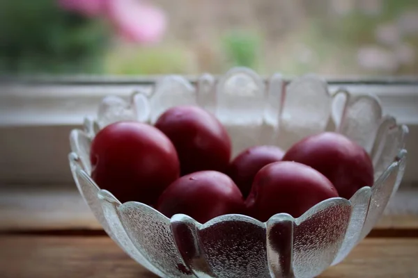 ripe plums in a crystal bowl on wooden background