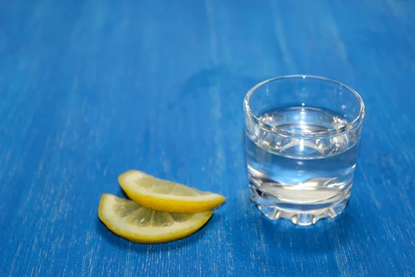 Alcoholic drink (vodka) with lemon on a blue wooden background. copy space, top view.