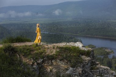 Doğada uzun sarı saçlı genç bir kız mesafeye bakar. Doğada sarı elbiseli bir kız. Ormanda, nehirde