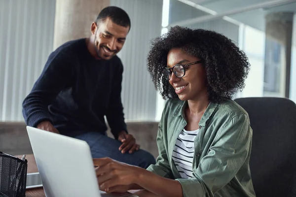 Yaratıcı bir Afrikalı iş kadını masasında otururken onun erkek meslektaşı için dizüstü bilgisayarda bir şey gösteren