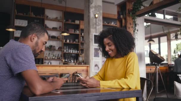 Pareja joven sentada en la cafetería usando su teléfono inteligente — Vídeos de Stock