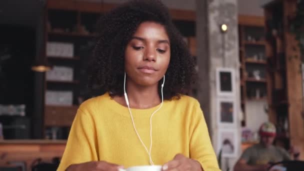 Mujer joven sosteniendo una taza de café escuchando música en los auriculares — Vídeos de Stock