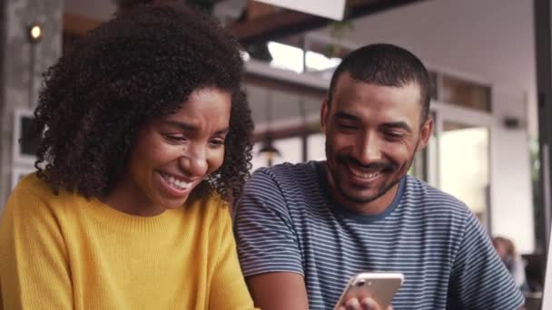 Счастливая молодая пара смотрит на мобильный телефон в кафе — стоковое видео