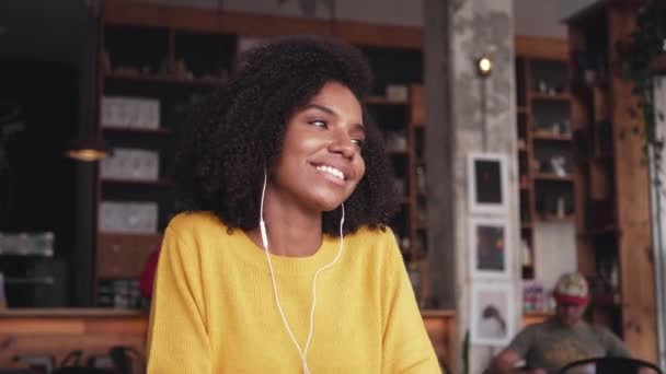 Mujer joven sonriente escuchando música en el auricular en la cafetería — Vídeos de Stock