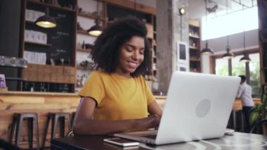 Kafede dizüstü bilgisayar kullanan genç bir kadın kahve içiyor.