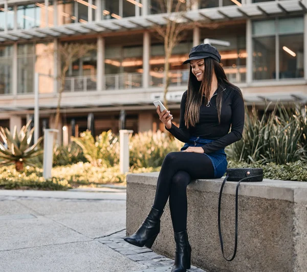 Mujer joven de moda sentada con bolsa de honda mirando su mo — Foto de Stock