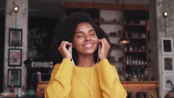 Fiatal nő egy kávézóban hallgat zenét a fülhallgató — Stock videók