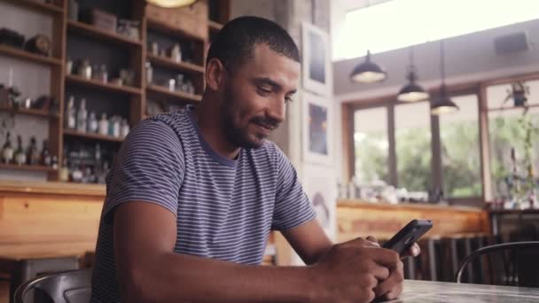 Un joven sentado en la cafetería de mensajes de texto en el teléfono móvil — Vídeos de Stock