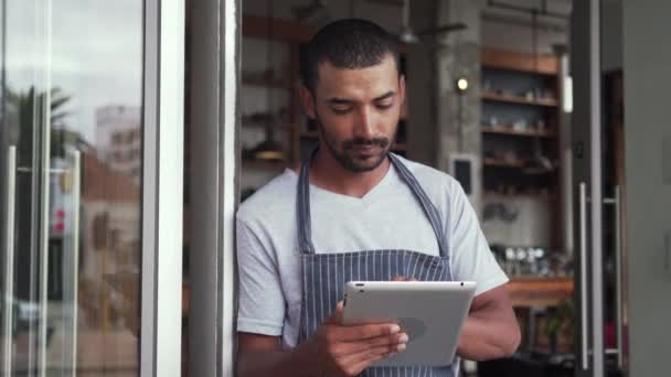 Kafenin kapısında dijital tablet tutan erkek sahibi duruyor — Stok video