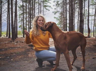Ormanda köpeğiyle oynayan gülümseyen genç kadın