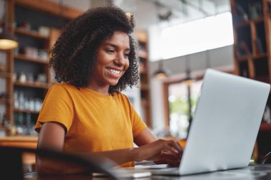 Kafede dizüstü bilgisayar kullanan mutlu genç siyah kadın