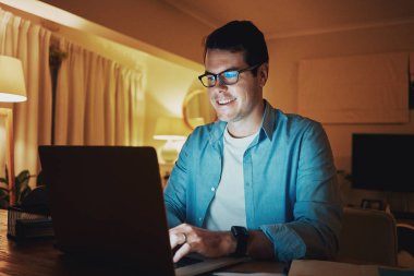 Smiling man enjoying surfing on laptop during late night clipart