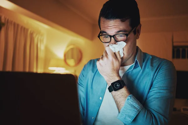 Sjuk man som täcker näsan med silkespapper arbetar sent på laptop — Stockfoto