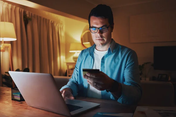 Чоловік використовує кредитну картку і ноутбук для оплати рахунків онлайн пізно вночі — стокове фото