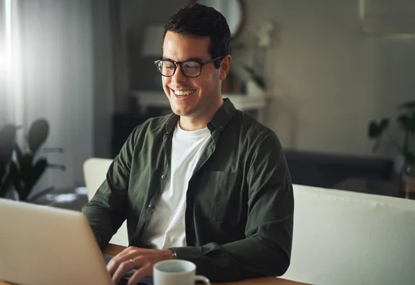Χαμογελαστός άνθρωπος κάθεται στο γραφείο στο σπίτι του δουλεύοντας σε φορητό υπολογιστή — Φωτογραφία Αρχείου