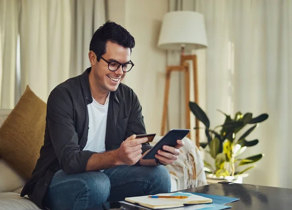 Fröhlicher Mann, der im Wohnzimmer sitzt und online per Kreditkarte einkauft — Stockfoto